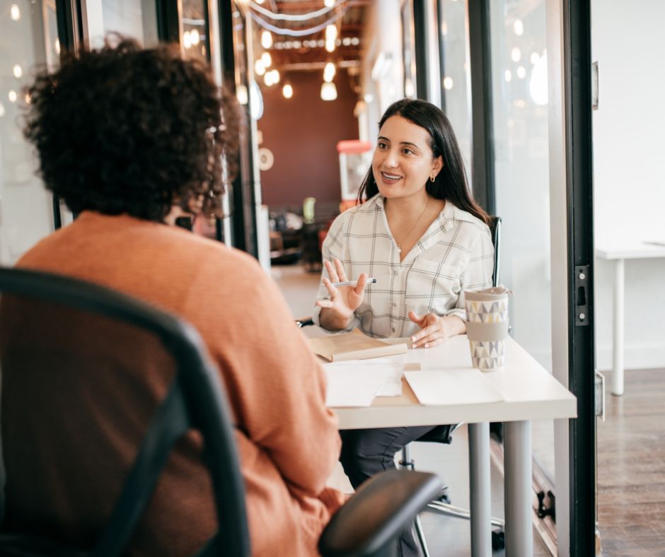 Two women having a friendly conversation in a modern office during a one-on-one meeting.