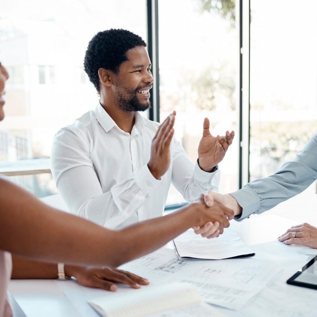 Man smiling and applauding while others shake hands during a successful meeting.