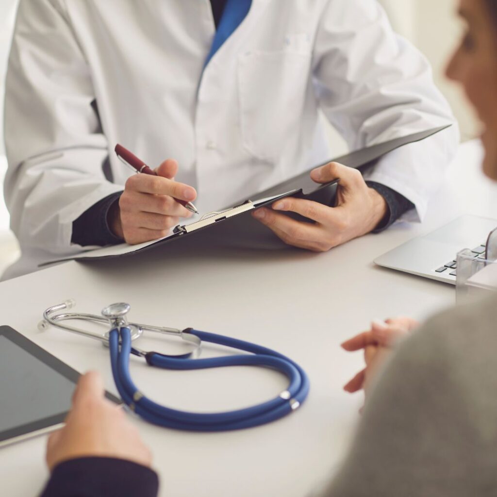 Doctor explaining notes on a clipboard to a patient, with a stethoscope on the table.