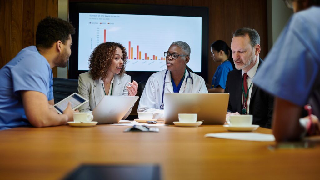 Medical professionals and administrators having a discussion during a meeting with a presentation screen.