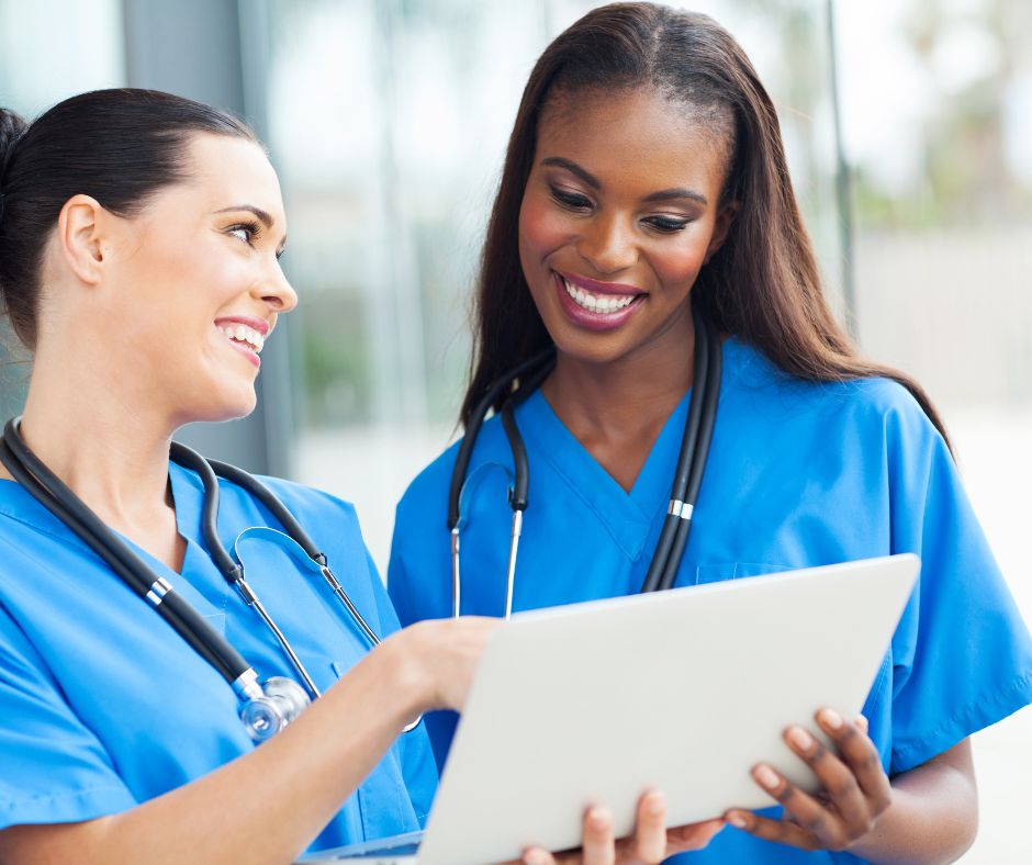 Two nurses smiling and discussing information displayed on a digital tablet.