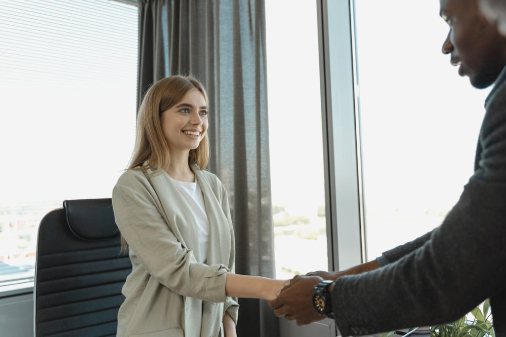 A female candidate shaking hands with a recruiter during a B2B sales hiring discussion in a professional office setting