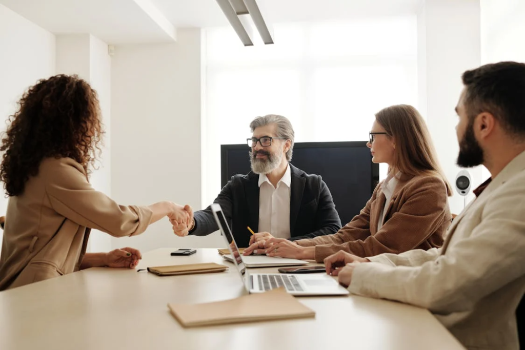 A group of recruiters meeting with a sales candidate, with one recruiter shaking hands to finalize a medical device sales hiring discussion