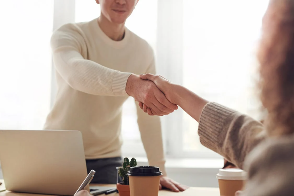 A male recruiter shaking hands with a candidate during a B2B sales hiring discussion at a professional meeting table