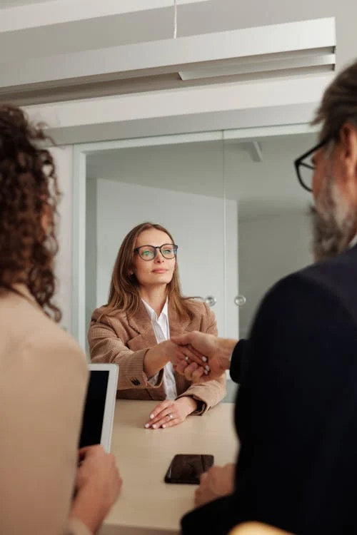 A recruiter shaking hands with a candidate during a B2B sales hiring discussion across a professional meeting table