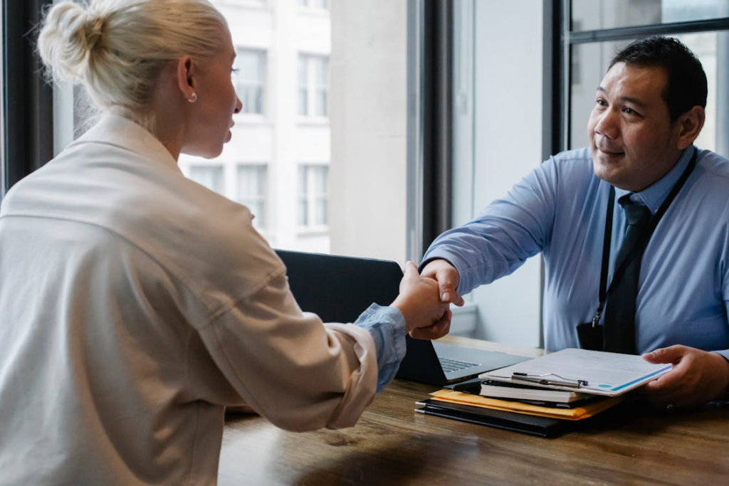 A recruiter shaking hands with a candidate during a medical device sales hiring meeting in a professional office setting